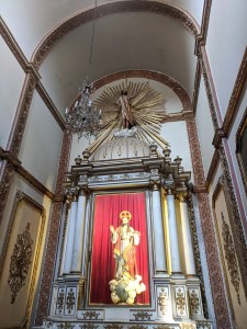 Religious statue wearing red robes against red drapery. 